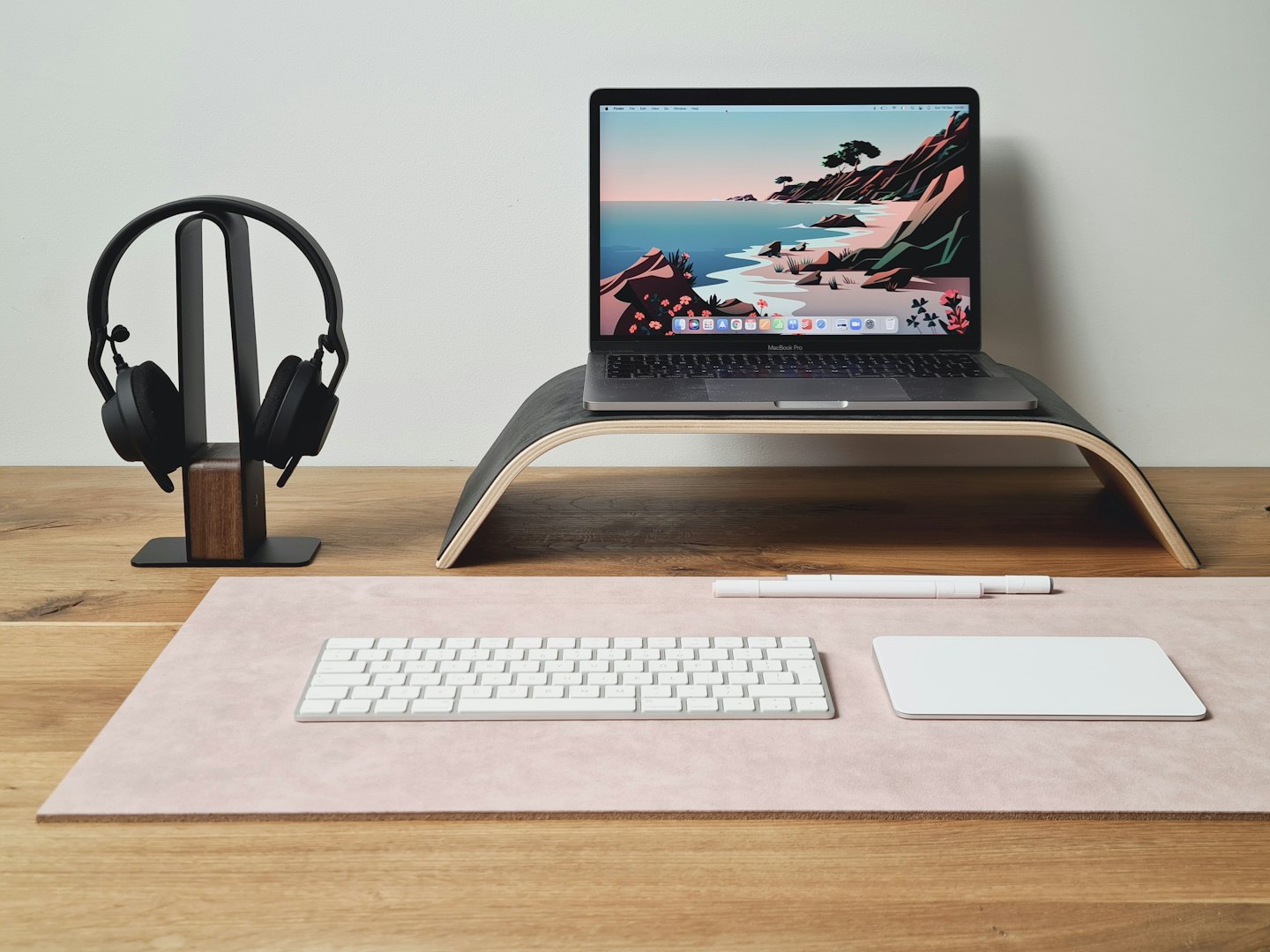 Laptop, hodetelefoner, tastatur og styreflate på et skrivebord.