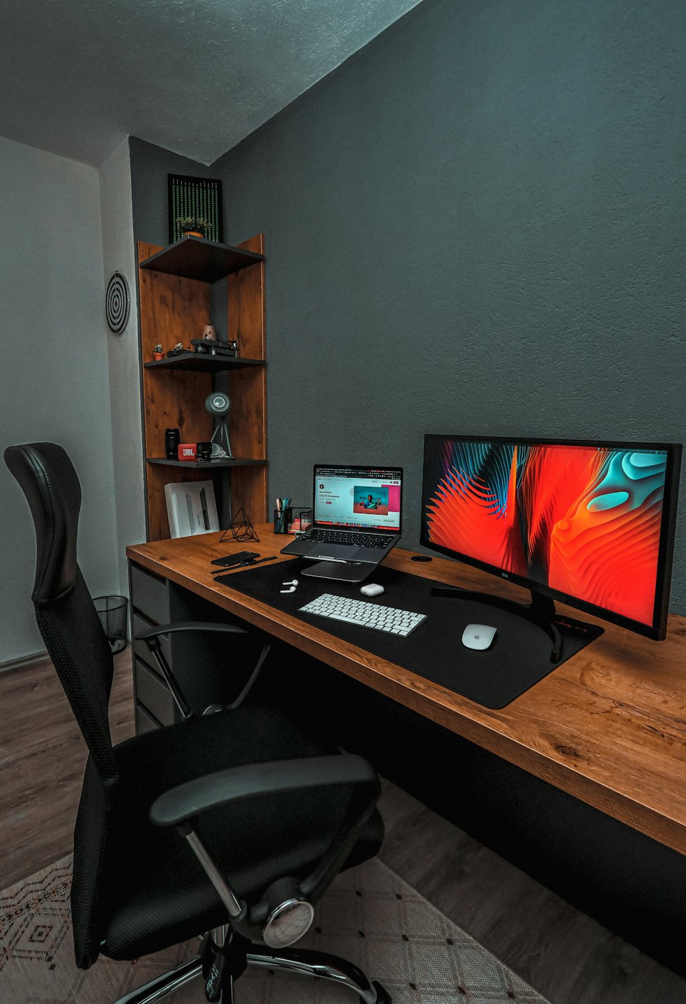 Laptop og skjerm på et skrivebord med en ergonomisk kontorstol.