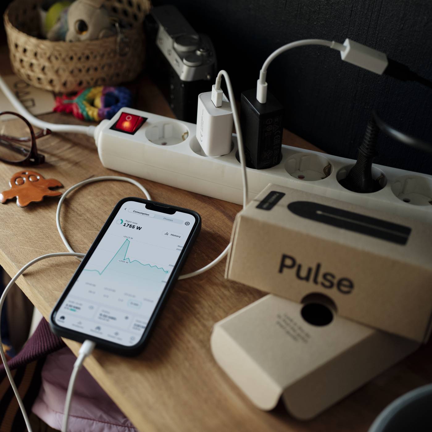 Tibber Pulse ved siden av en mobil som viser strømforbruket i sanntid